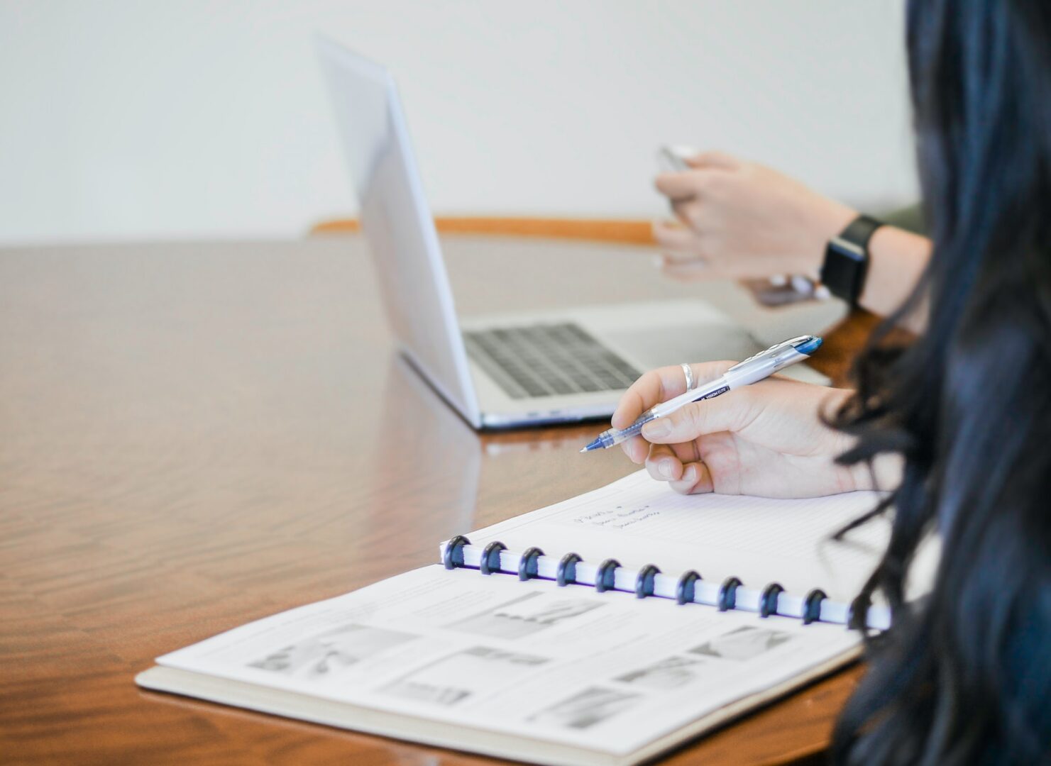 A person is writing on paper with a laptop in front of them.