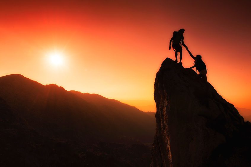 Two people climbing a rock at sunset.