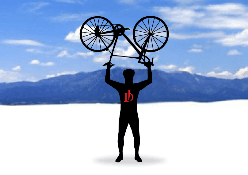 A man holding up a bicycle in front of mountains.
