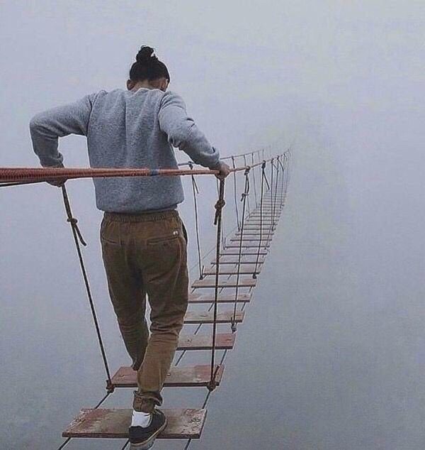 A man walking across a bridge in the fog.
